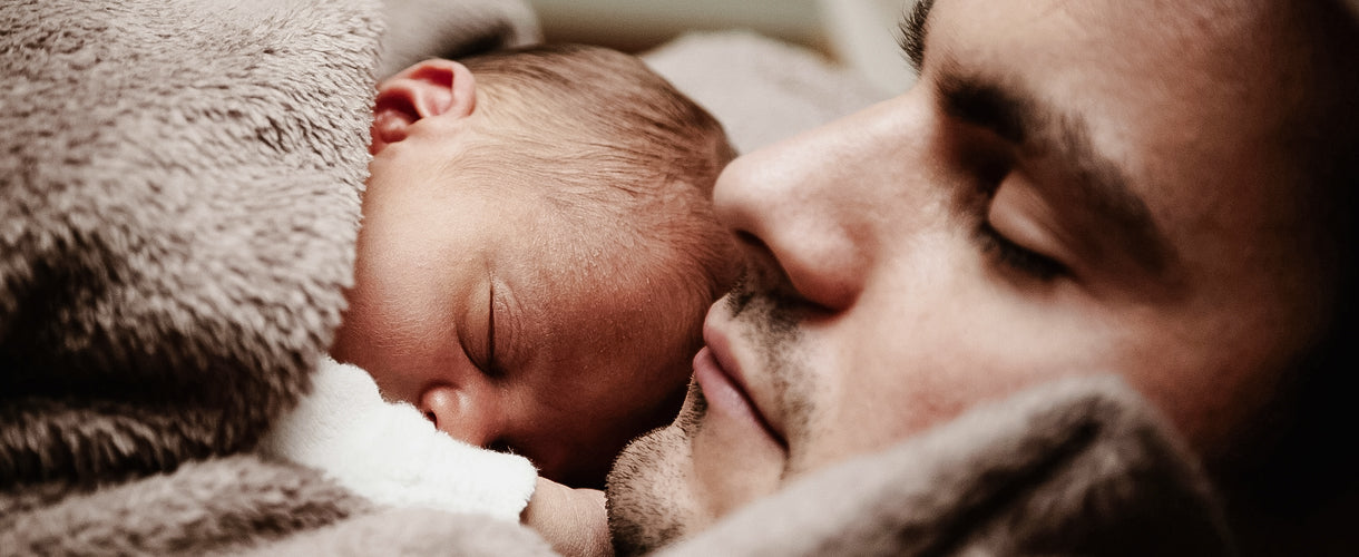 Newborn baby sleeping peacefully on their father's chest, both wrapped in a soft blanket, symbolising warmth, bonding, and the quiet beauty of early parenthood.