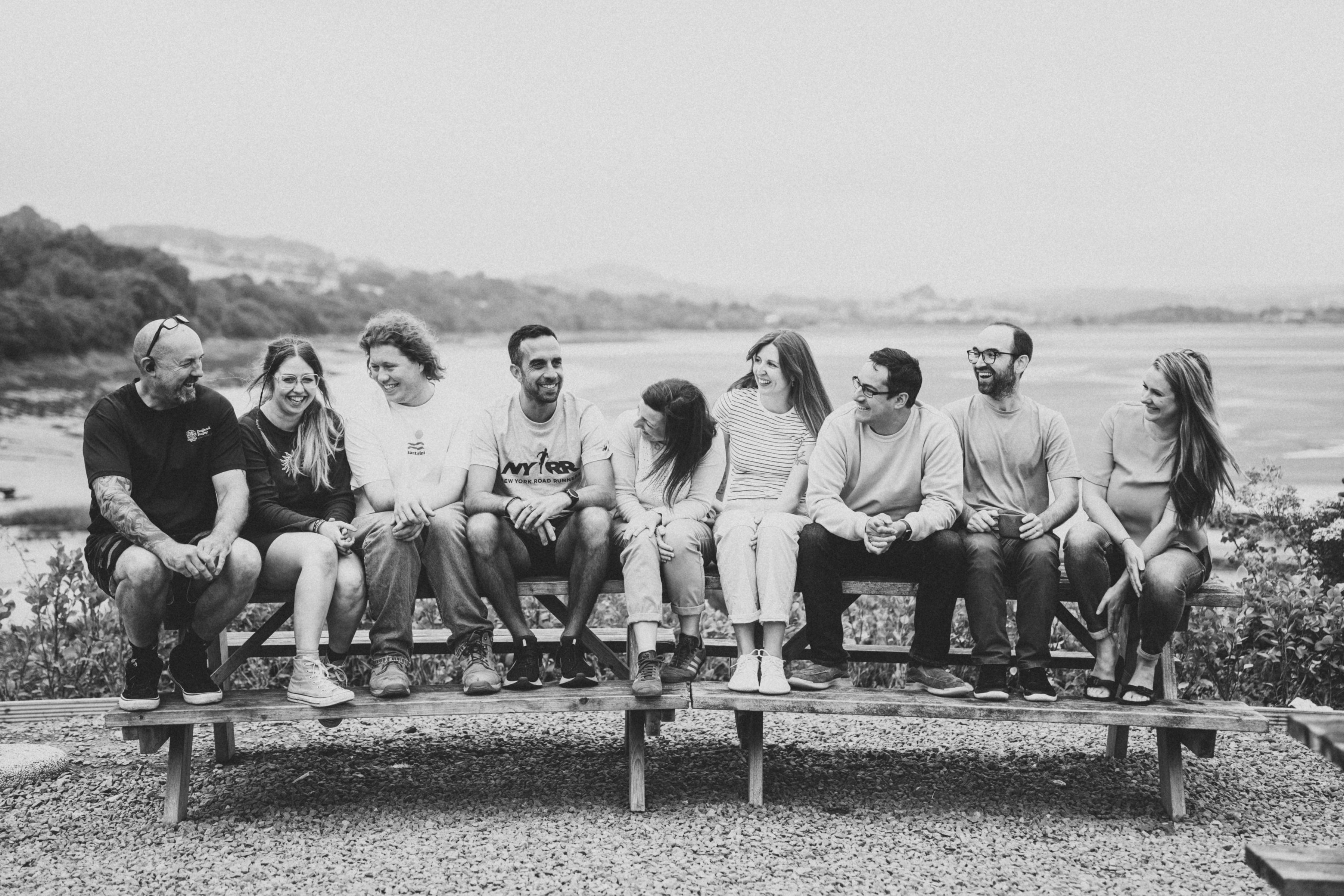 The Letterfest team sitting together on a bench, smiling and laughing outdoors with a scenic riverside background