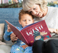An older woman is reading a personalized Christmas story book titled 'A Christmas Wish' to a young child who appears to be enjoying the story.