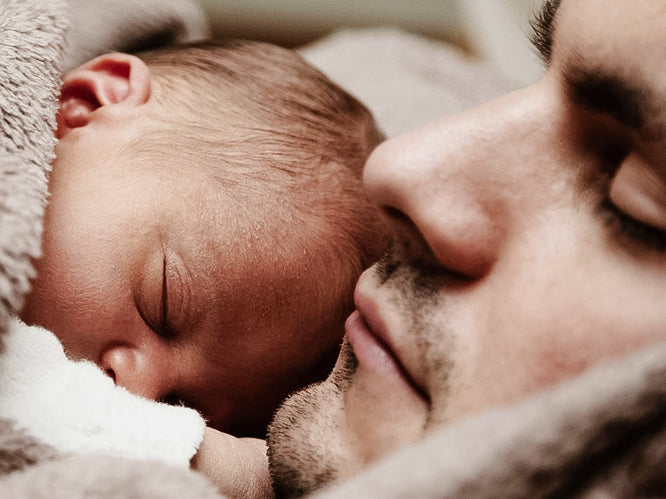 Newborn baby sleeping peacefully on their father's chest, both wrapped in a soft blanket, symbolising warmth, bonding, and the quiet beauty of early parenthood.