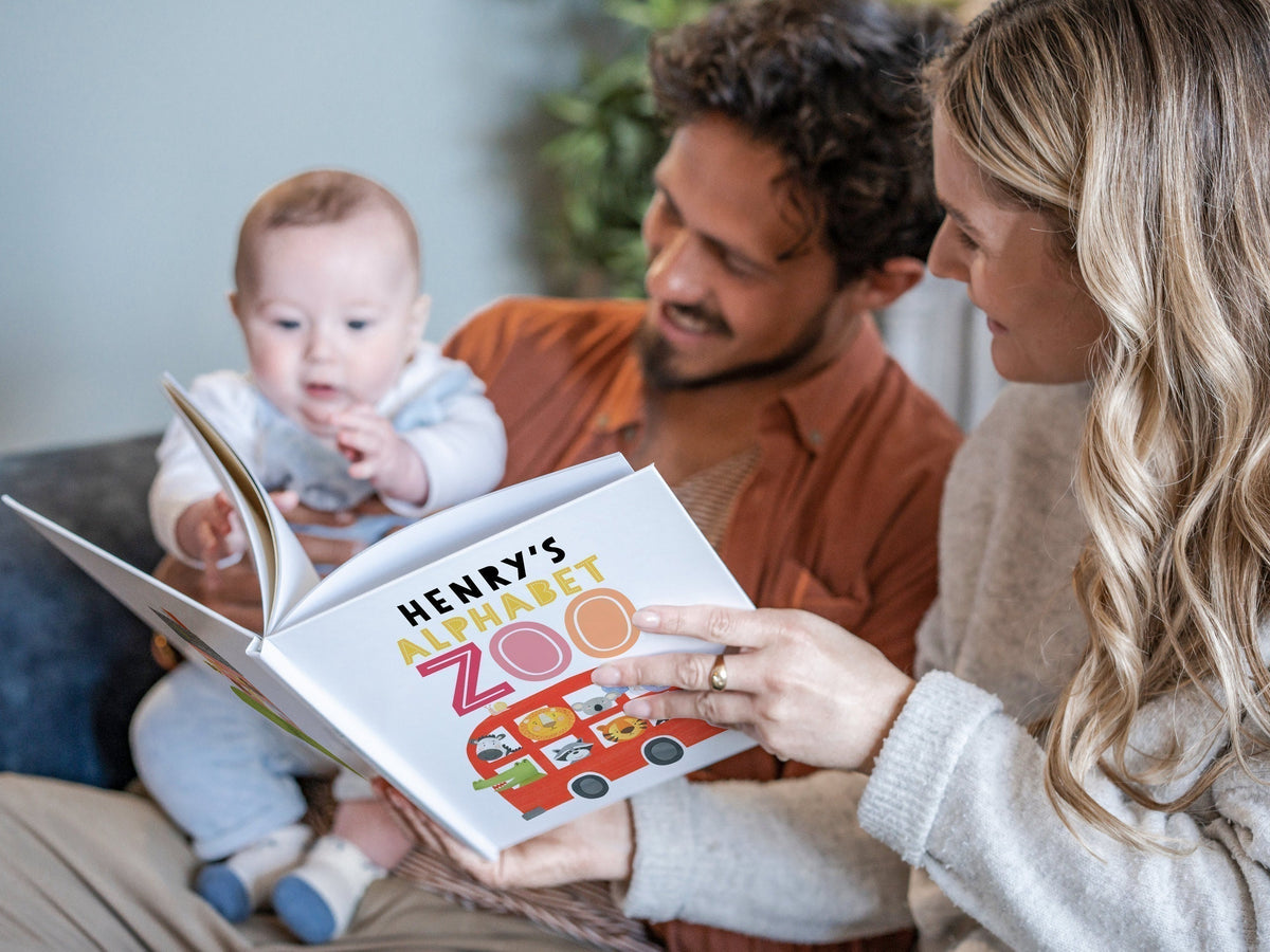 A couple reads a personalised book, "Henry’s Alphabet Zoo," to their baby, who reaches for the pages with curiosity.