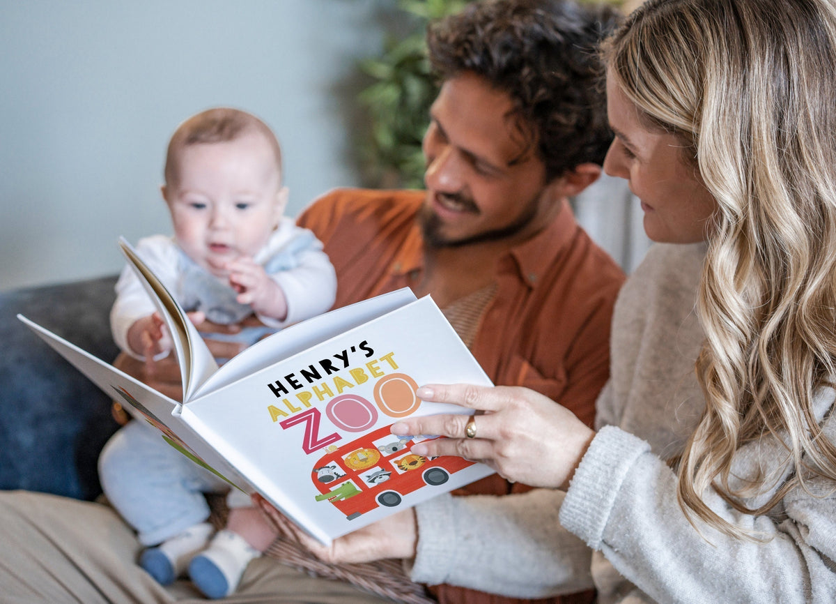 A couple reads a personalised book, "Henry’s Alphabet Zoo," to their baby, who reaches for the pages with curiosity.