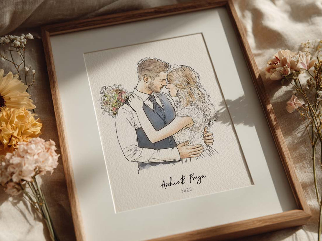 Framed personalised wedding portrait of a couple embracing, surrounded by dried flowers on soft linen bedding