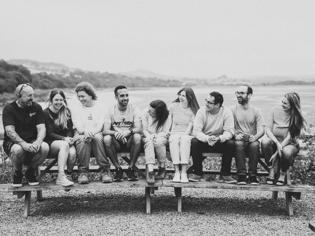 The Letterfest team sitting together on a bench, smiling and laughing outdoors with a scenic riverside background
