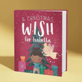 Book titled 'A Christmas Wish for Isabella' with illustrations of a child, angel, and Christmas tree on a red background.